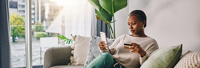 Shot of a young woman using her card and phone to shop online at home